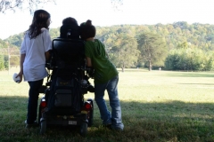 child-leaning-against-sisters-wheelchair-looking-across-field