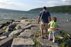 dad-helps-daughter-with-leg-braces-over-rocks-by-lake